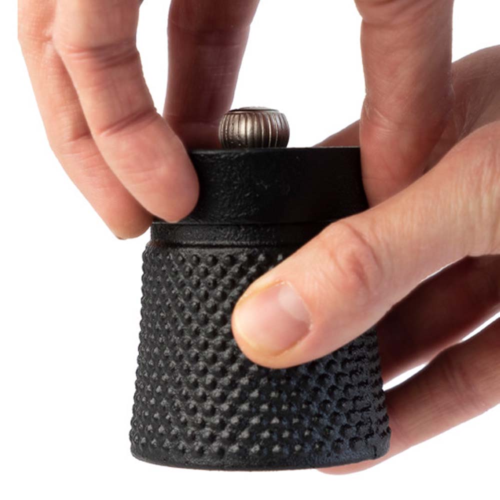 Peugeot Bali Fonte black cast iron pepper mill on a white background with hands turning mill