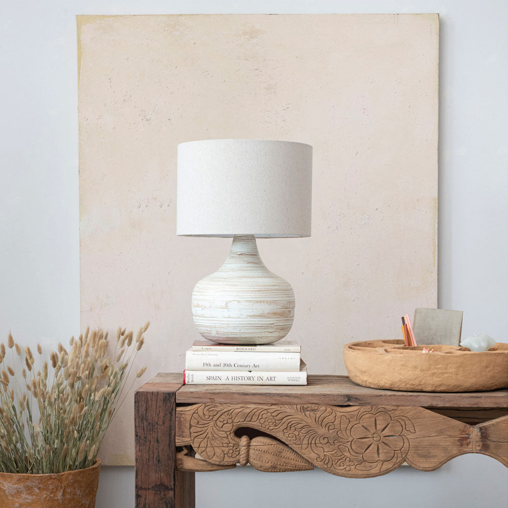 Lamp with whitewashed bamboo base and linen shade on a stack of books set on a wood console