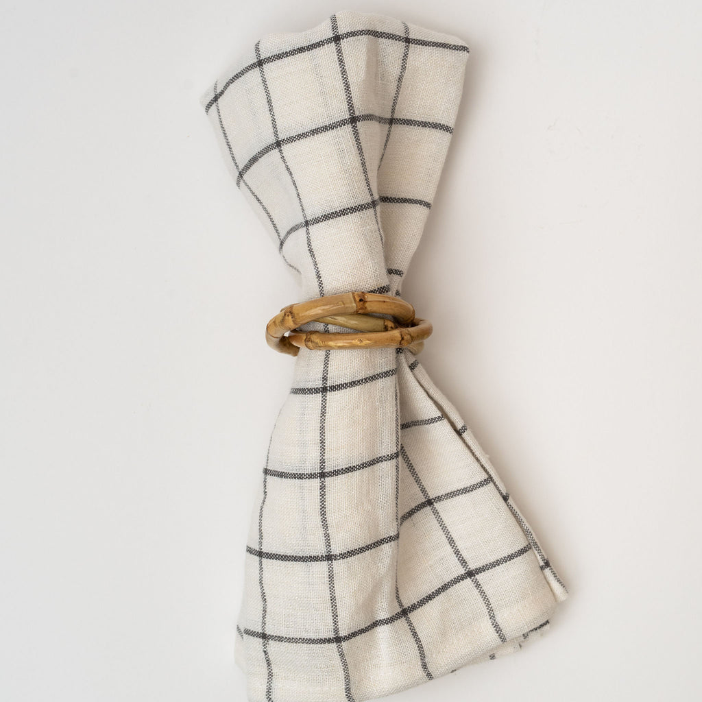 Bamboo napkin rings with three interlocking rinds on a linen napkin on a white background