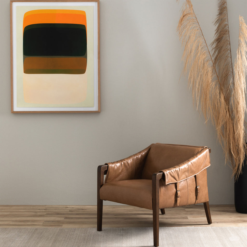 Four Hands Furniture brand Bauer chair in taupe leather with stained wood legs and leather buckled straps in a room with dried grass and a modern painting hanging on a grey wall