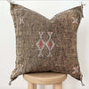 Brown throw pillow with tribal embroidered pattern on a stool with a white background
