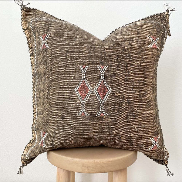 Brown throw pillow with tribal embroidered pattern on a stool with a white background