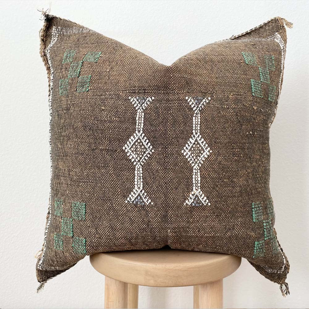 Close up of Brown throw pillow with tribal embroidered pattern on a stool with a white background