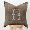Close up of Brown throw pillow with tribal embroidered pattern on a stool with a white background