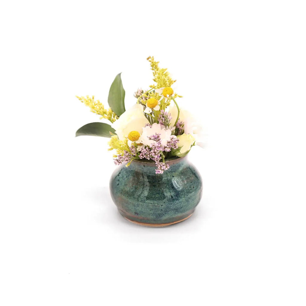 Small blue pottery bud vase with flowers on a white background