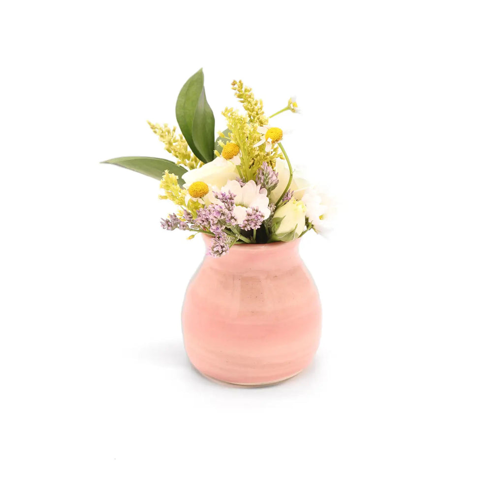 Small pink pottery bud vase with flowers on a white background