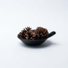 Black terracotta bowl with short handle and pinecones on a white background