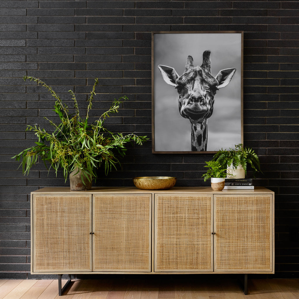 Four Hands furniture brand Carmel side board with four cane doors and metal legs in front of a black wall with photograph of a giraffe above