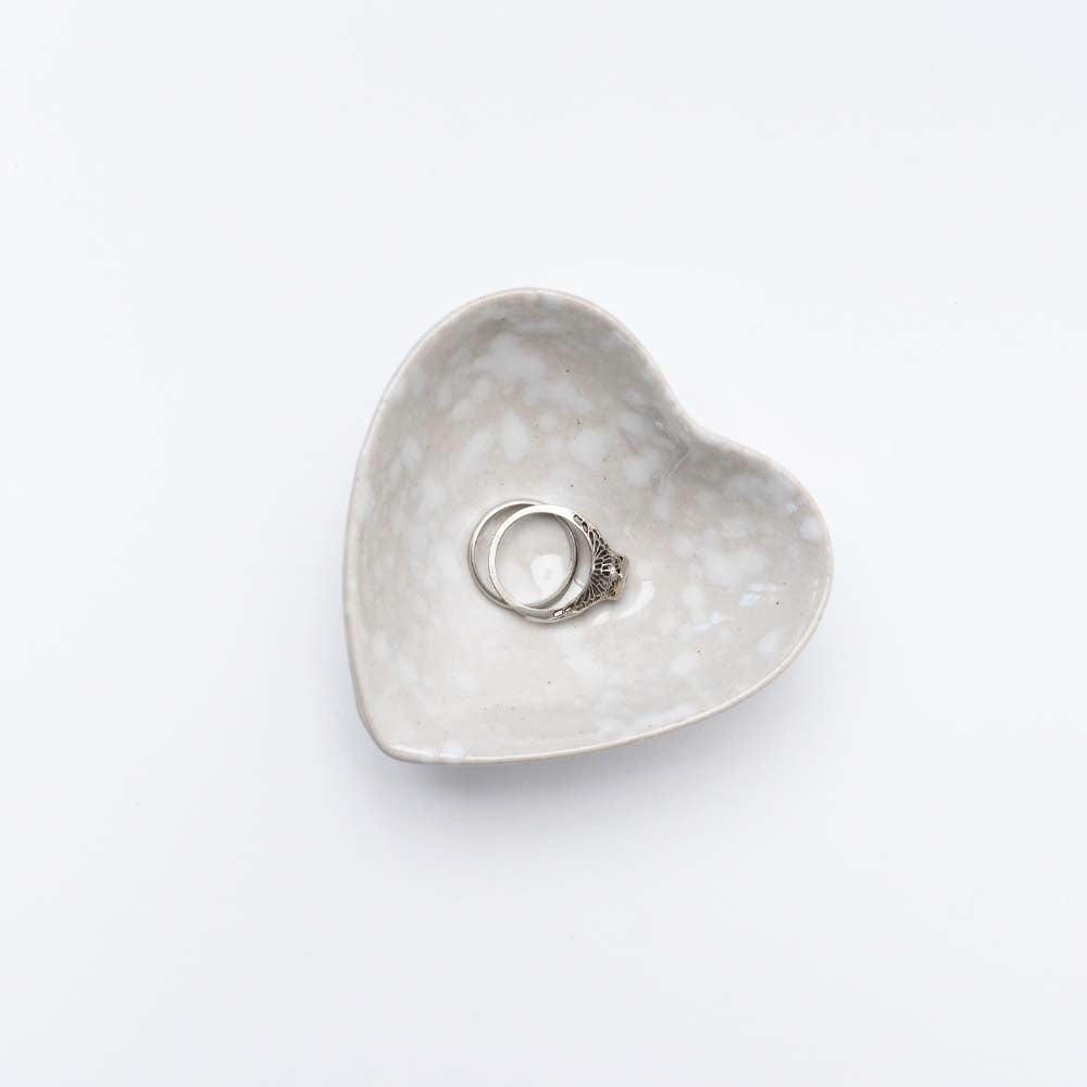 Close up of Decorative white stoneware heart dish on a white background with rings inside