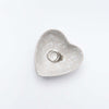 Close up of Decorative white stoneware heart dish on a white background with rings inside