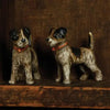 Two cast iron terrier figurines on a wood shelf
