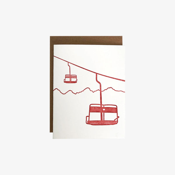 White greeting card with two red chairlifts imprinted via letter press one with small carved heart in back
