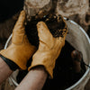Person with bucket and soil wearing yellow leather garden work gloves 