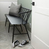 Black metal bench with Windsor chair styling and curves back rail in a mudroom with tile floor and pair of sneakers nearby