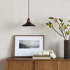 Black leather and walnut pendant light with black cord above wood sideboard with picture leaning and large black vase with greenery