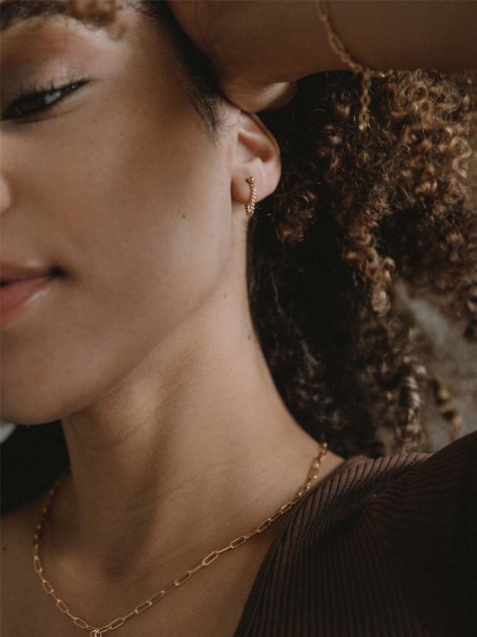 Model wearing Able brand Curb Chain earrings in 14 carat gold fill on a grey background  Edit alt text