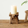 Small wood pedestal with four legs and a candle on top on top of a wood table