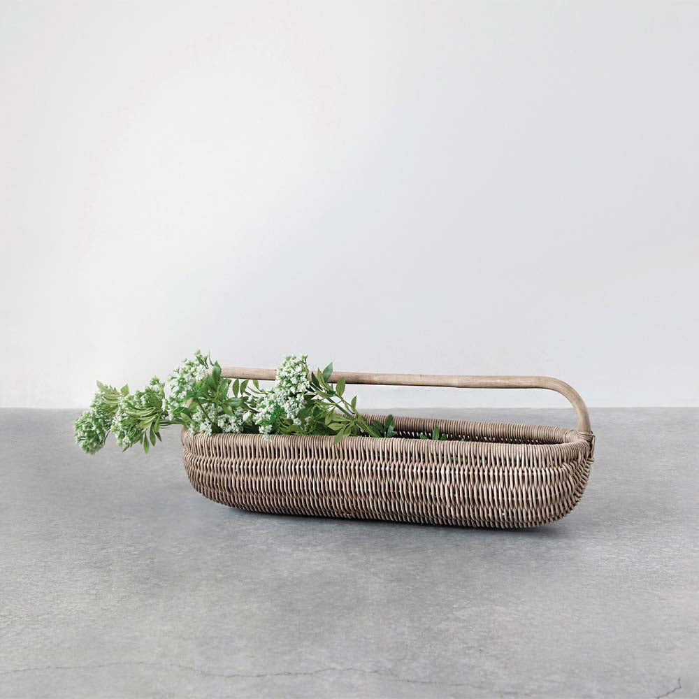 Long rattan basket with green and white flowers on a stone surface