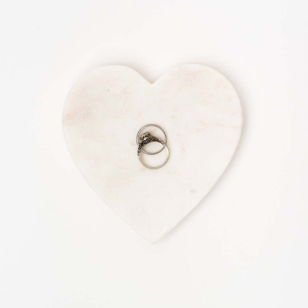 Small white marble heart dish with two rings on a white background