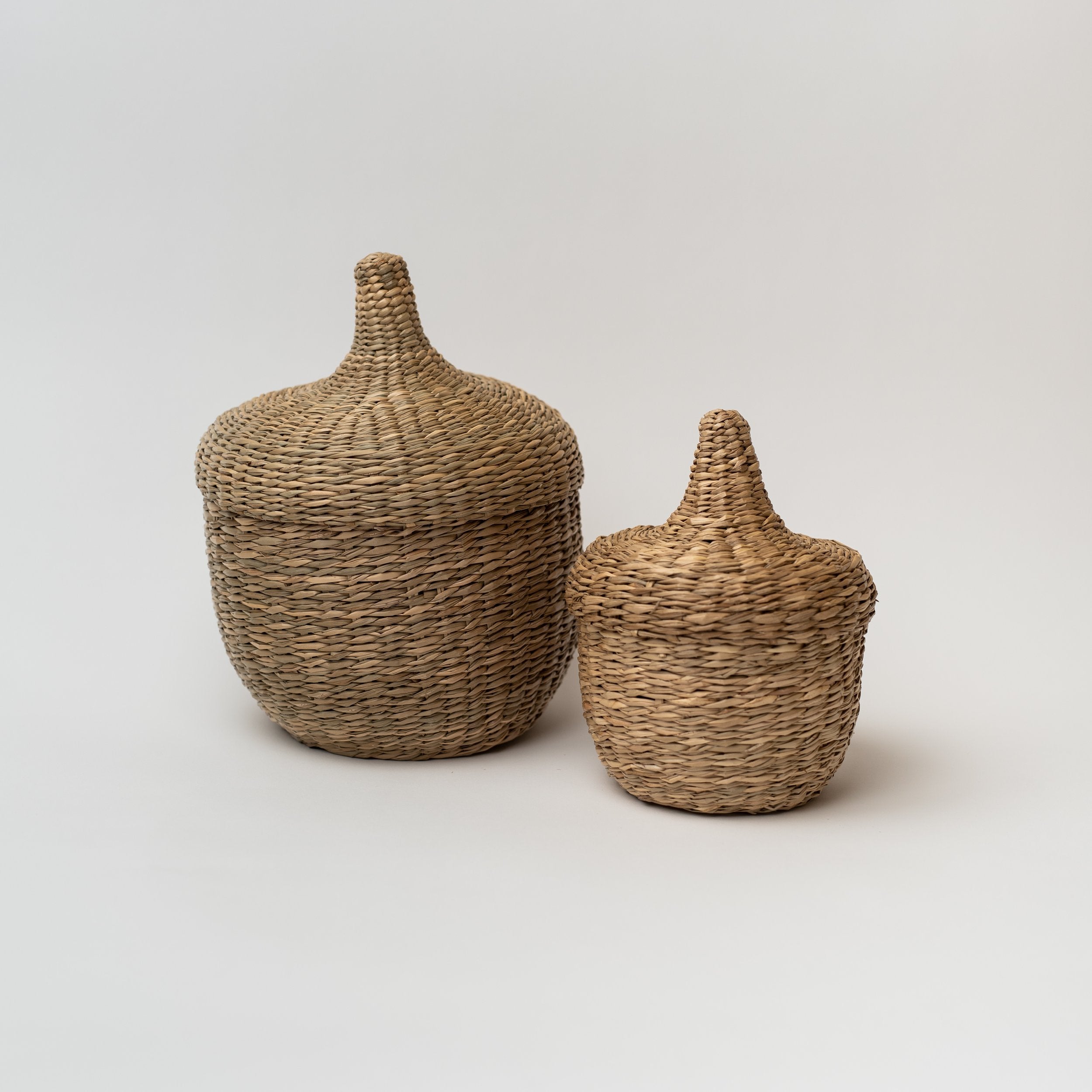 Two seagrass baskets with lids that look like acorns on a white background