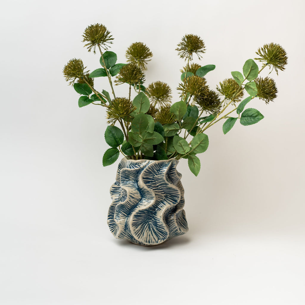 Cream vase with blue flutter patterns and greenery inside on a white background