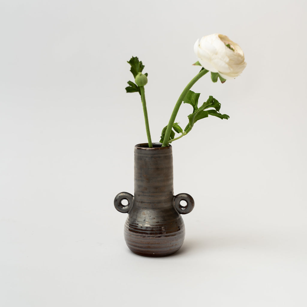 Black bud vase with loop accents holding a white flower on a. white background