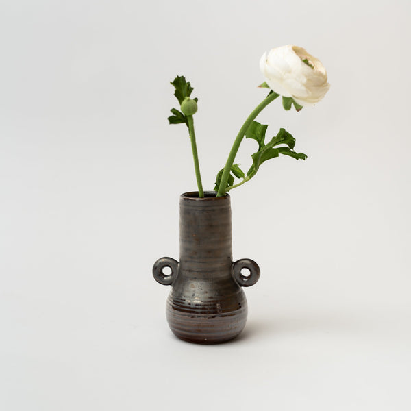 Black bud vase with loop accents holding a white flower on a. white background