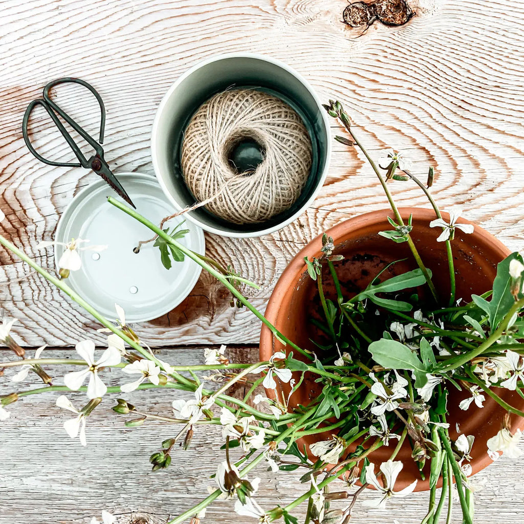 garden twine dispenser with ball of twin on a wood table next to pot and flowers