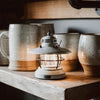 White mini Edison lantern by Barebones brand with vintage style and caged bulb on a shelf with mugs