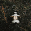 White mini Edison lantern by Barebones brand with vintage style and caged bulb hanging in an evergreen tree 