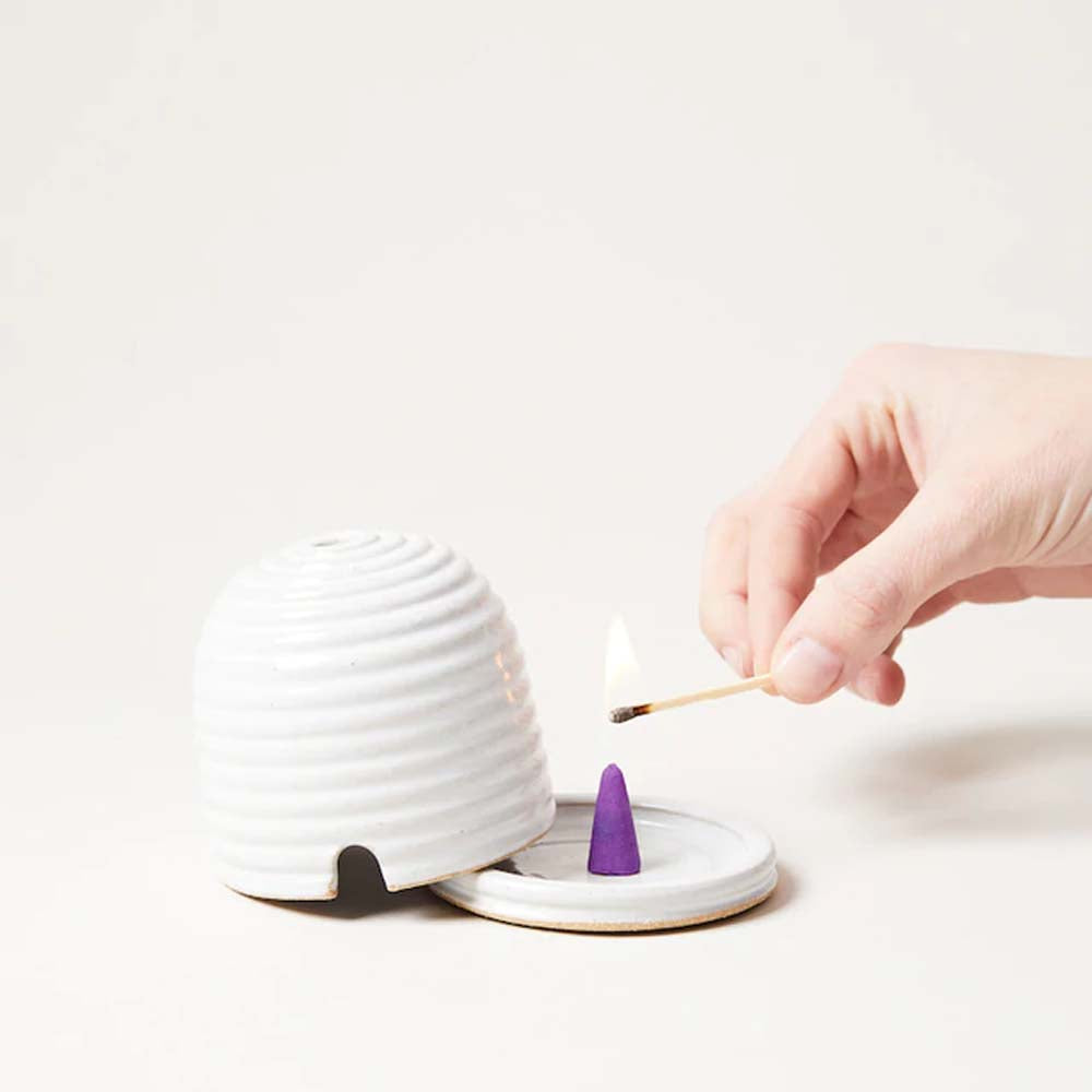 Farmhouse Pottery Beehive Burner being lit with a hand and match on a white background