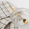 Pressed glass footed bowl with brass spoon and checked napkin on a white background