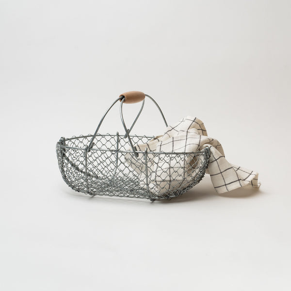 Wire basket with wood handle with plaid towel on a white background