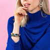 Model wearing blue sweater and stack of ink + alloy brand colorful stretch bracelets on a pink background