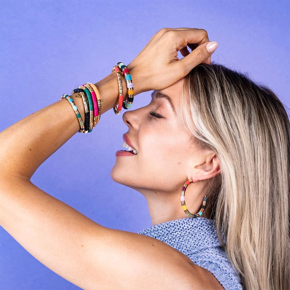 Model wearing stack of colorful ink and alloy stretch bracelets on a purple background