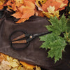 Barebones brand garden shears with ambidextrous black and wood handle on a leather matt among leaves