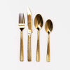 Stainless steel brass colored flatware set of four pieces on a white background