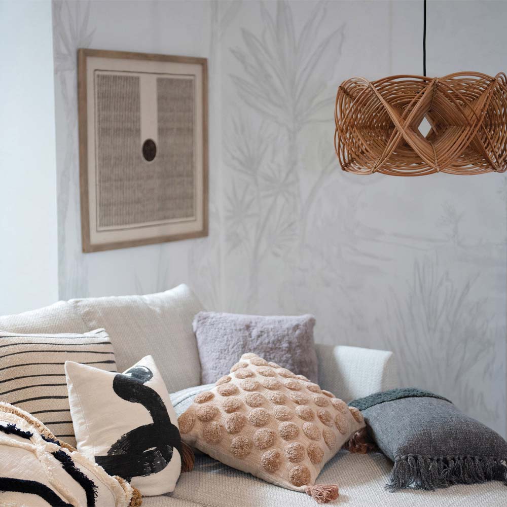 Rattan woven pendant with large bulb and black cord over a sofa with pillows 