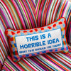 Needlepoint pillow by Furbish brand with bright colors and phrase 'this is a horrible idea what time should I be there' on brightly striped chair
