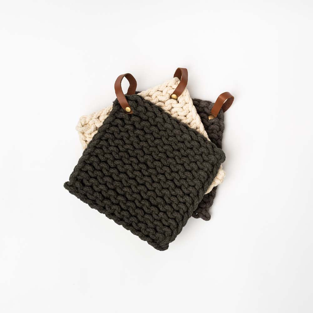Thick crocheted pot holders in charcoal and creme with leather loops stacked an a white background