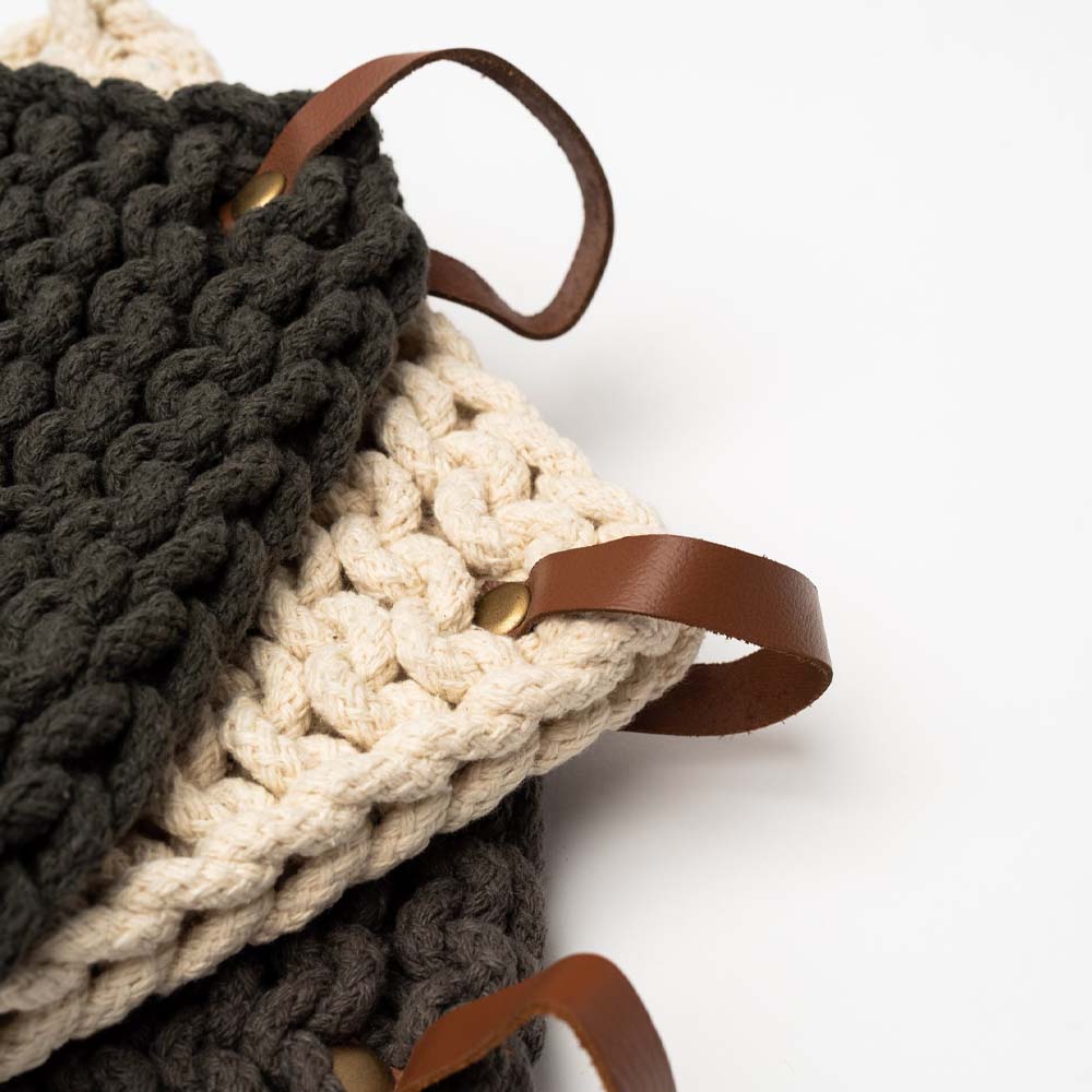 Closeup Thick crocheted pot holders in charcoal and creme with leather loops stacked an a white background