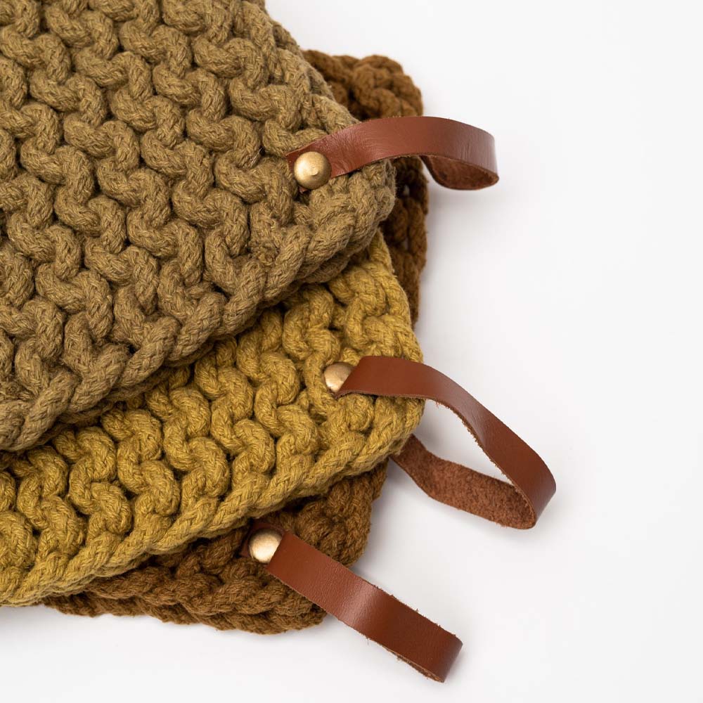 Mustard colored crocheted pot holders in fall colors with leather loops stacked an a white background