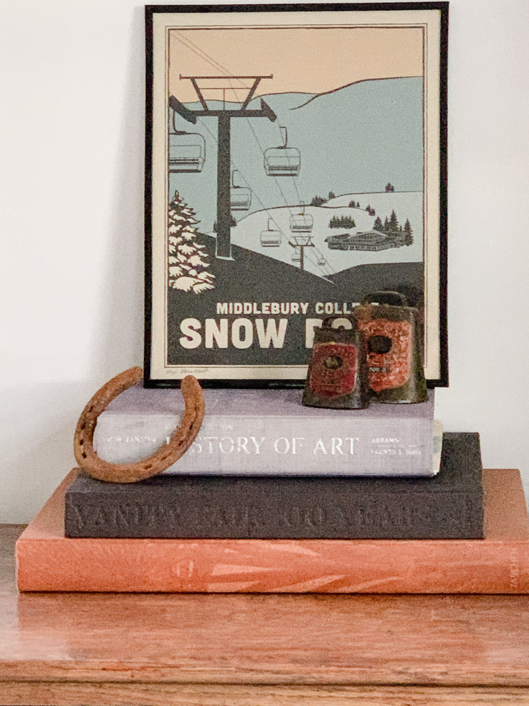 Framed wood cut style print of the chairlift at Middlebury College Snow Bowl with books and cow bell 