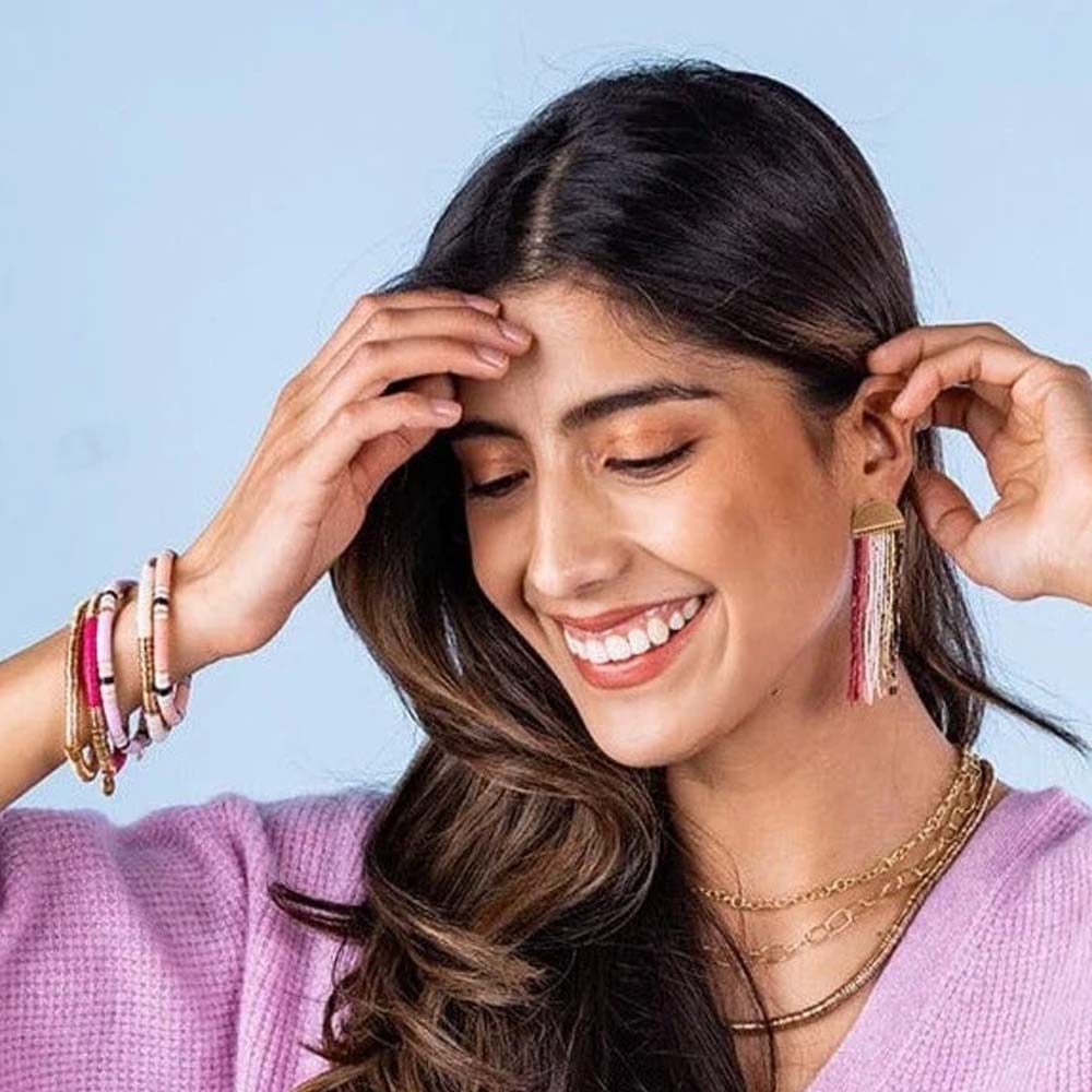 Model wearing purple sweater and collection of pink and gold ink and alloy brand stretch bracelets in front of a blue background