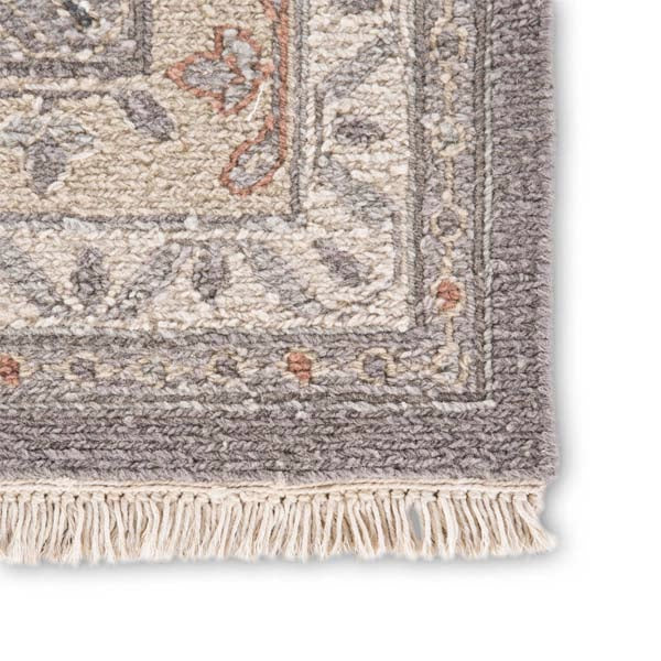 Close up of Jaipur wool JAIMAK rug with Pops of gold and dusty pink on gray backdrop with classic fringe