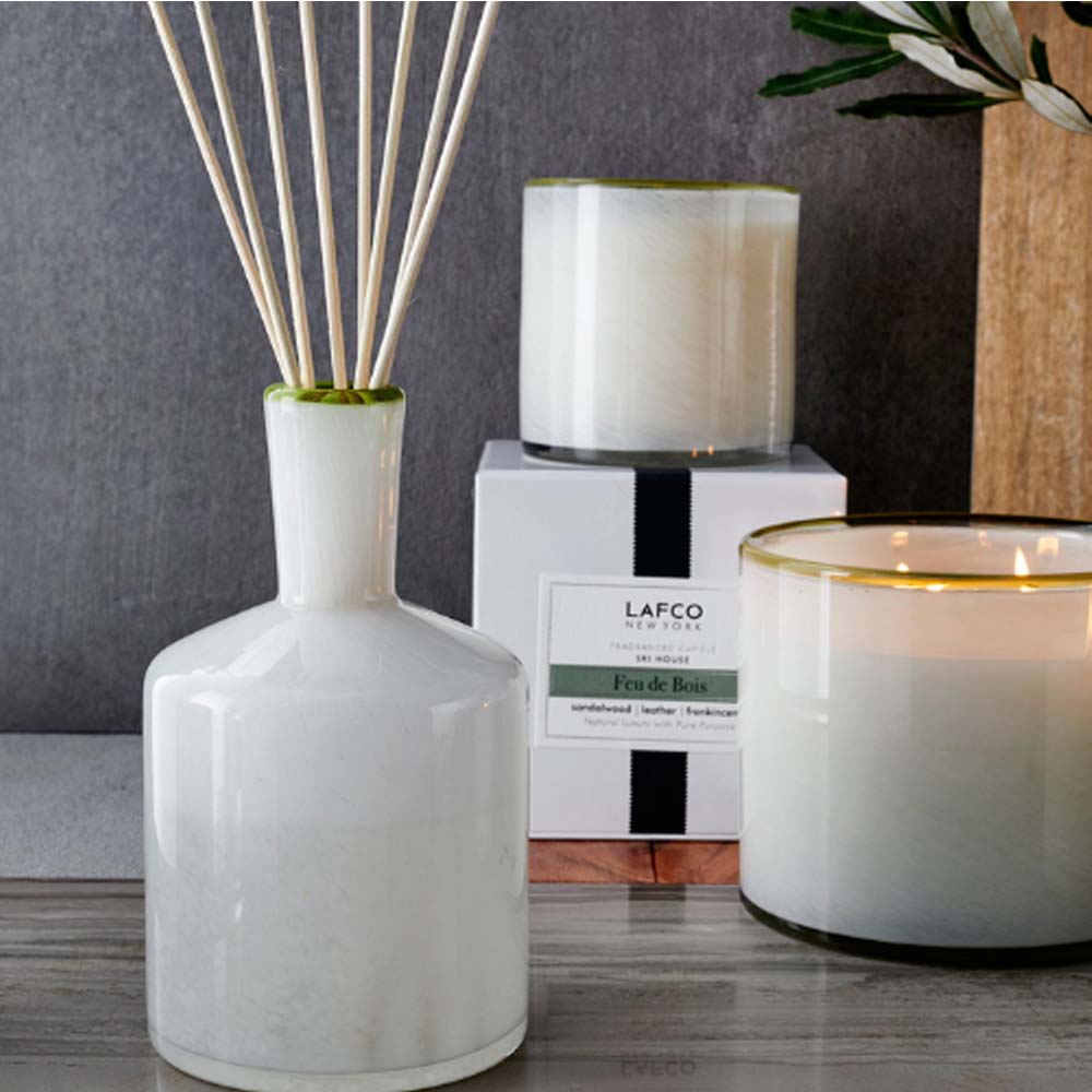 Lafco brand white glass feu de bois reed diffuser and candles on a wood surface