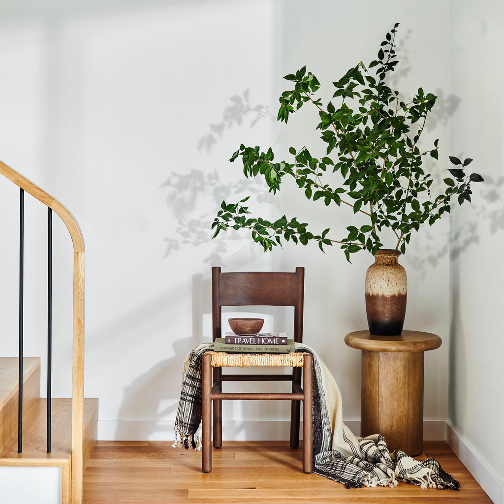 Staircase landing with wood side table with vase and greenery beside four hands furniture largo dining chair in russet