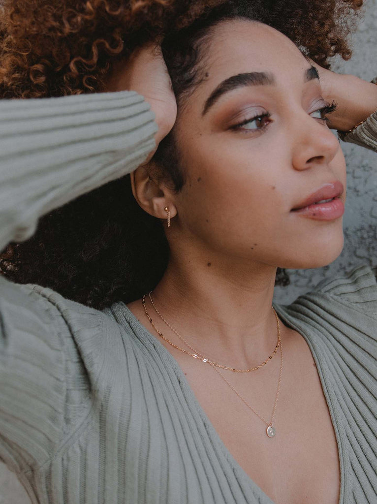 Able jewelry gold layered necklace with two chains and circle pendant on woman with dark hair and gray v-neck sweater