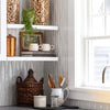 Sunny white kitchen with grey counter and shelves with crocks and books and plant 