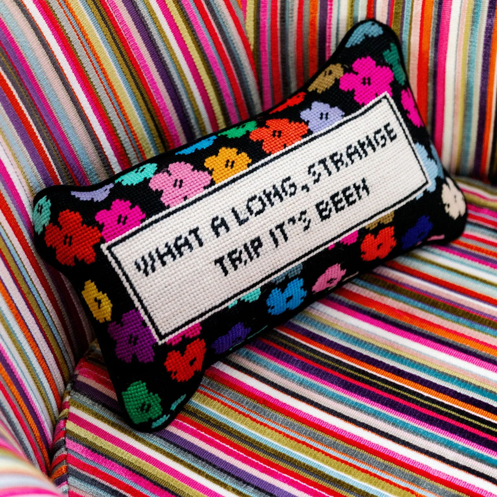 Needlepoint pillow by Furbish brand with bright colors and phrase 'what a long strange trip its been' on a striped cushion